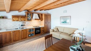 A kitchen with wooden cabinets, a stove, and a sink. There is a beige sofa and a dining table with chairs.