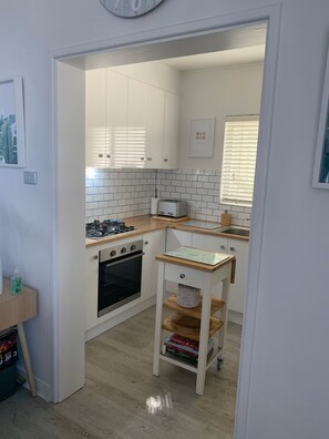 Eine kompakte Küche mit weißen Schränken, einem Gasherd, einem Backofen, einem Toaster und einem kleinen Tisch mit einem Korb.