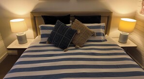 Una cama con ropa de cama a rayas, dos lámparas de noche y varias almohadas.