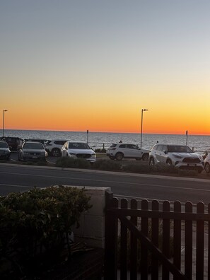 Ein Parkplatz mit parkenden Autos entlang einer Straße, mit Blick auf ein Gewässer bei Sonnenuntergang.