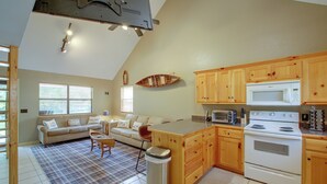A compact kitchen with wooden cabinets, a microwave, a stove, and a dining area with a plaid rug. - Lake & Dock Access! Waterfront Hot Springs Haven (Hot Springs)