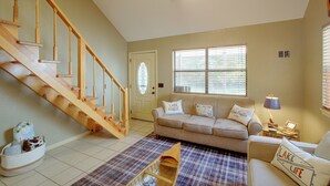 A living room with a wooden staircase, a beige sofa, a plaid rug, and a window with blinds. - Lake & Dock Access! Waterfront Hot Springs Haven (Hot Springs)