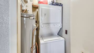 Een kleine wasruimte met een wasmachine en droger, een metalen rek en een plank met diverse spullen.