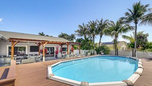 A wooden deck with a swimming pool, a covered patio area, and palm trees. - Walk to Water! Boynton Beach Gem w/ Backyard Oasis (Boynton Beach)