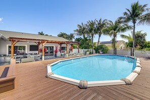 Eine Holzterrasse mit Swimmingpool, überdachter Veranda und Palmen.