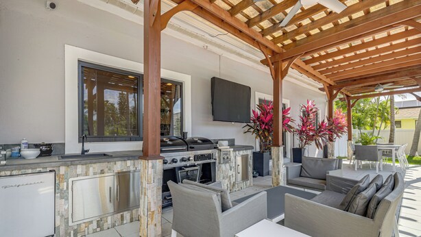 An outdoor kitchen with a grill, seating area, and a TV mounted on the wall. - Walk to Water! Boynton Beach Gem w/ Backyard Oasis (Boynton Beach)