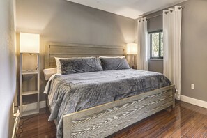 Ein Schlafzimmer mit einem Bett, Nachttischen, einem Fenster mit Vorhängen und einem Beistelltisch.