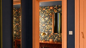Een gang met een spiegel, een deur en een kaptafel met bloemenbehang.