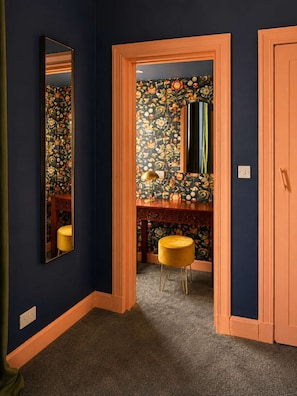 Ein Flur mit Spiegel, Tür und Schminktisch mit floralem Wandpapier.
