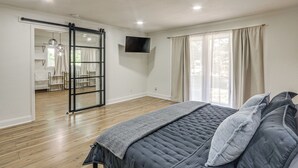 A bedroom with a bed, a sliding door to a bathroom, a mounted TV, and a window with curtains. - Great for Youth Sports Trips! Roomy Goddard Home (Goddard)