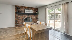 A dining area with a brick fireplace, a wooden table, and white chairs. - Great for Youth Sports Trips! Roomy Goddard Home (Goddard)