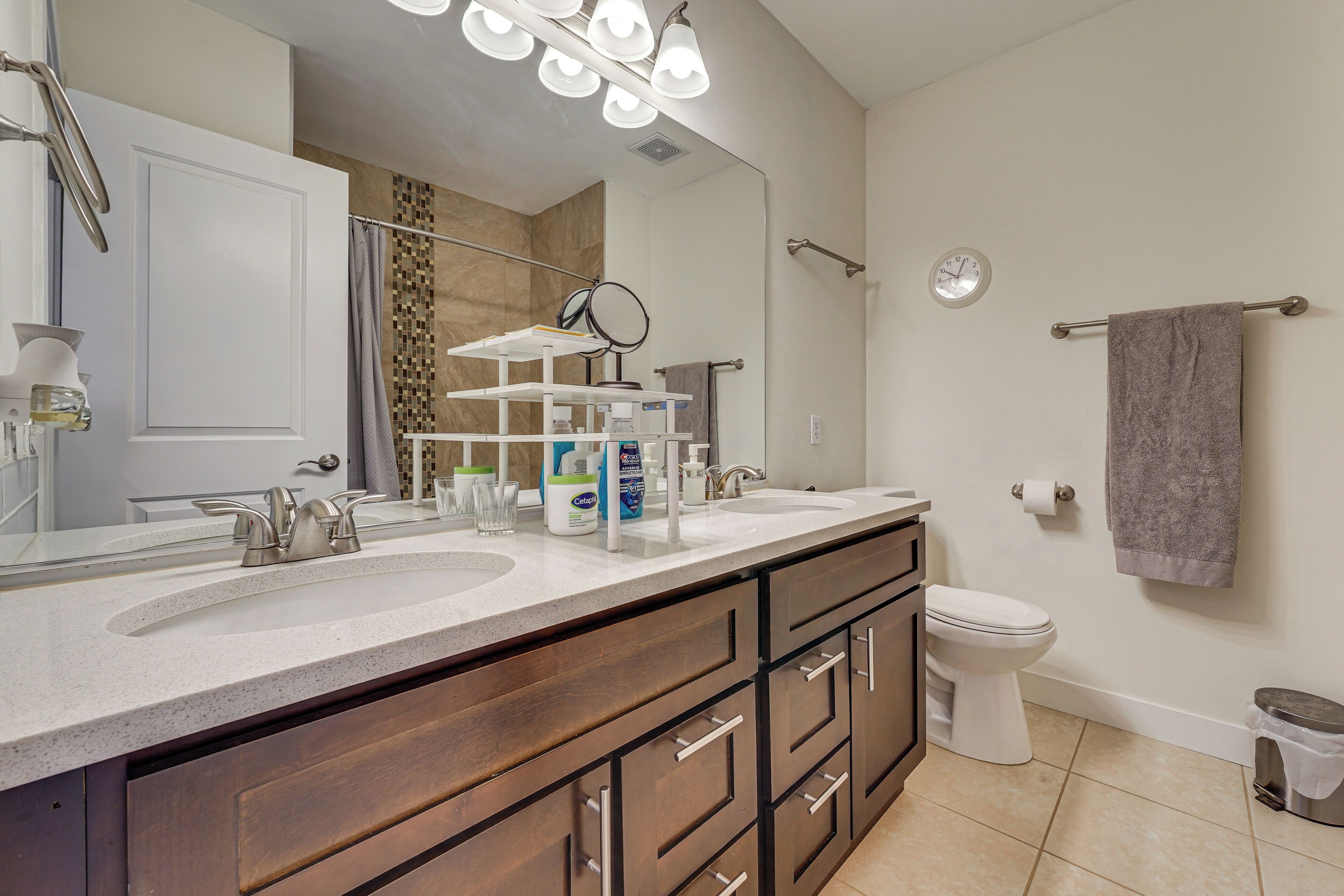 A bathroom with a double sink, a mirror, a towel rack, and a toilet.