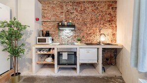 Una cocina compacta con pared de ladrillo, microondas, lavamanos y horno pequeño.