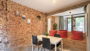 Una habitación con pared de ladrillo, un banco de madera con cojines rojos, una mesa con sillas y una lámpara colgante.