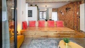 Una sala de estar moderna con una plataforma de madera, cojines rojos y una pared de ladrillo.