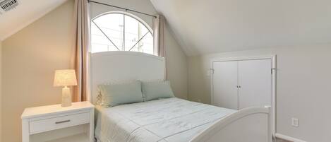 A bedroom with a bed, a nightstand, a lamp, a window with curtains, and a door.