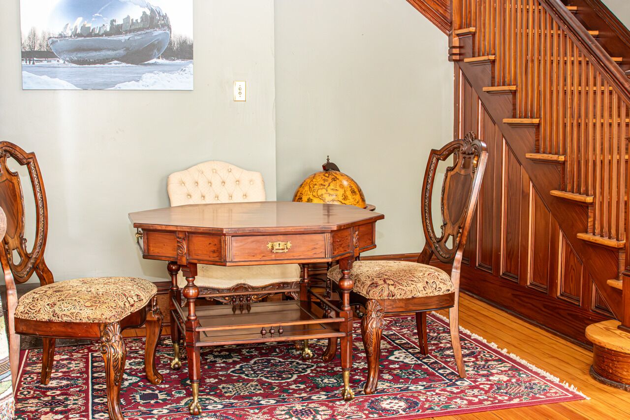 Un espace repas avec une table et des chaises en bois, un tapis à motifs et un escalier.