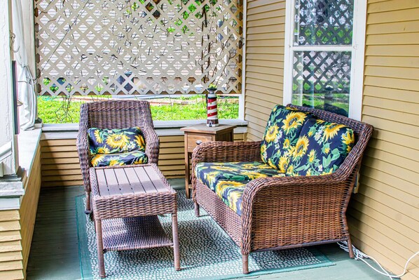 A wicker sofa and chair with floral upholstery, a small table, and a decorative lighthouse ornament on a windowsill.