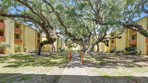 A courtyard with a paved walkway, trees, and yellow buildings with balconies. - Dock Access! Condo 5 Mi to Okaloosa Island Beach (Mary Esther)