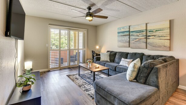 A living room with a gray sofa, a coffee table, a ceiling fan, and a TV mounted on the wall. - Dock Access! Condo 5 Mi to Okaloosa Island Beach (Mary Esther)