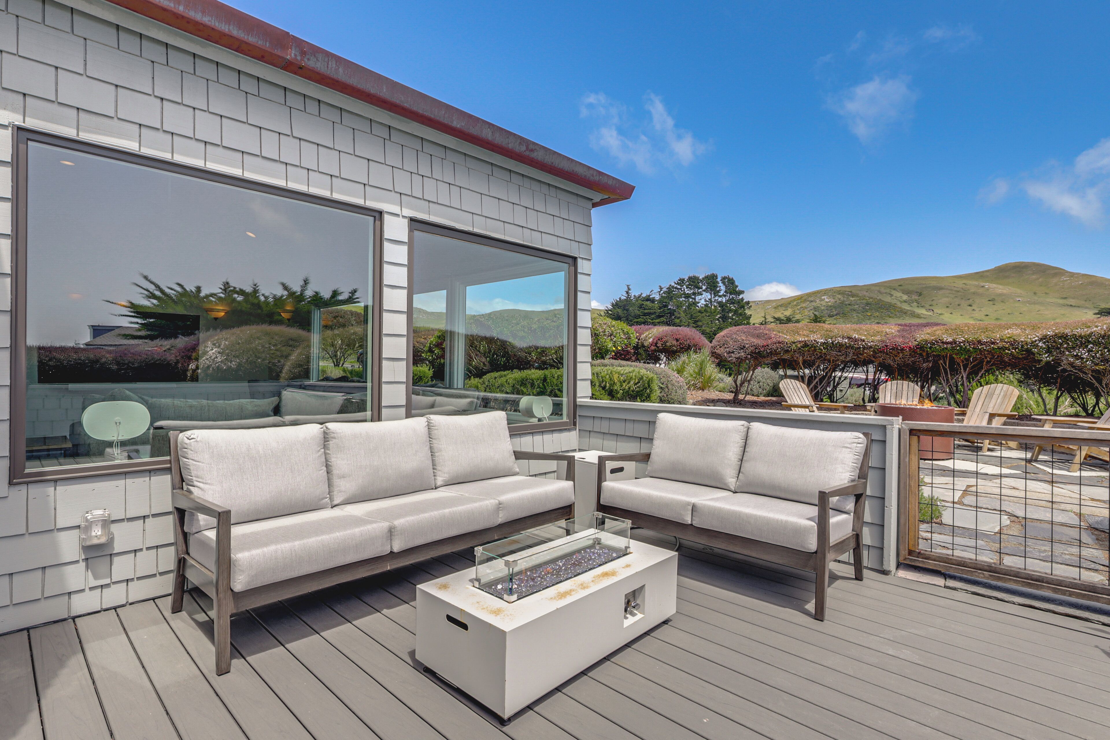 Eine Terrasse mit einer Sitzecke, einem Glastisch und Blick auf eine hügelige Landschaft.