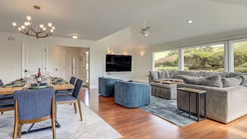 A modern living room with a dining area, a grey sofa, and a chandelier.