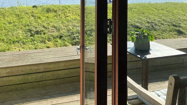 Eine Holzterrasse mit einer Glastür, die zu einem Blick auf ein Gewässer führt.