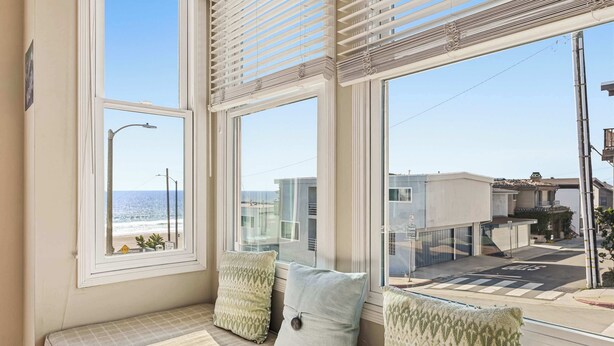 A room with a view of the beach, a bench with pillows, and a window with blinds. - Ocean View Manhattan Beach Townhome | Steps to Beach (Manhattan Beach)