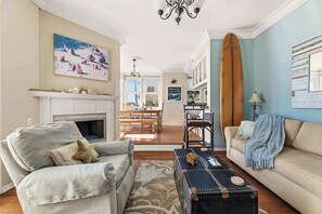 A living room with a fireplace, a dining area, and a surfboard. - Ocean View Manhattan Beach Townhome | Steps to Beach (Manhattan Beach)