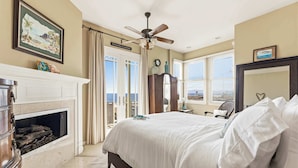 A bedroom with a bed, a fireplace, a ceiling fan, and a view of the ocean through the window. - Ocean View Manhattan Beach Townhome | Steps to Beach (Manhattan Beach)