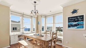 A dining area with a wooden table and benches, large windows, and a wall-mounted sign. - Ocean View Manhattan Beach Townhome | Steps to Beach (Manhattan Beach)