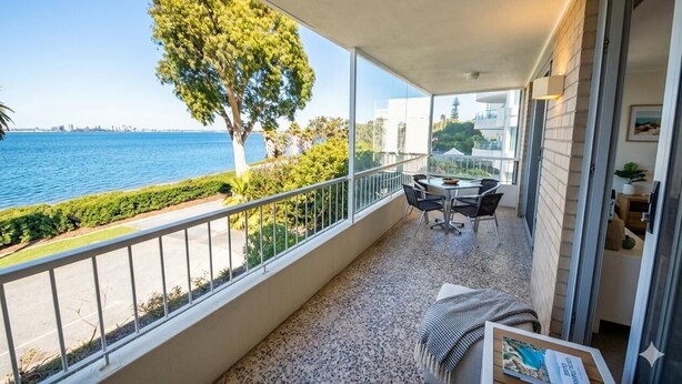 A balcony with a table and chairs, a view of the sea, and a tree.