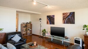 A living room with a leather sofa, a glass coffee table, a flat-screen TV, a bookshelf, and a floor lamp.