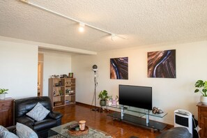 A living room with a leather sofa, a glass coffee table, a flat-screen TV, a bookshelf, and a floor lamp.