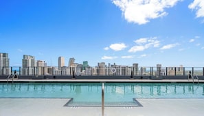 Piscina no terraço com vista para o horizonte da cidade, grades de metal e placas indicando 'EXIT'.