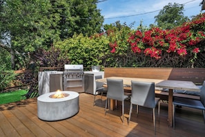 Eine Terrasse im Freien mit Grill, Esstisch, Stühlen und einem Feuerkorb.