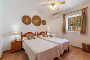 Ein Schlafzimmer mit zwei Betten, einem Deckenventilator, einem Fenster mit Vorhängen und einer Wand-Klimaanlage.