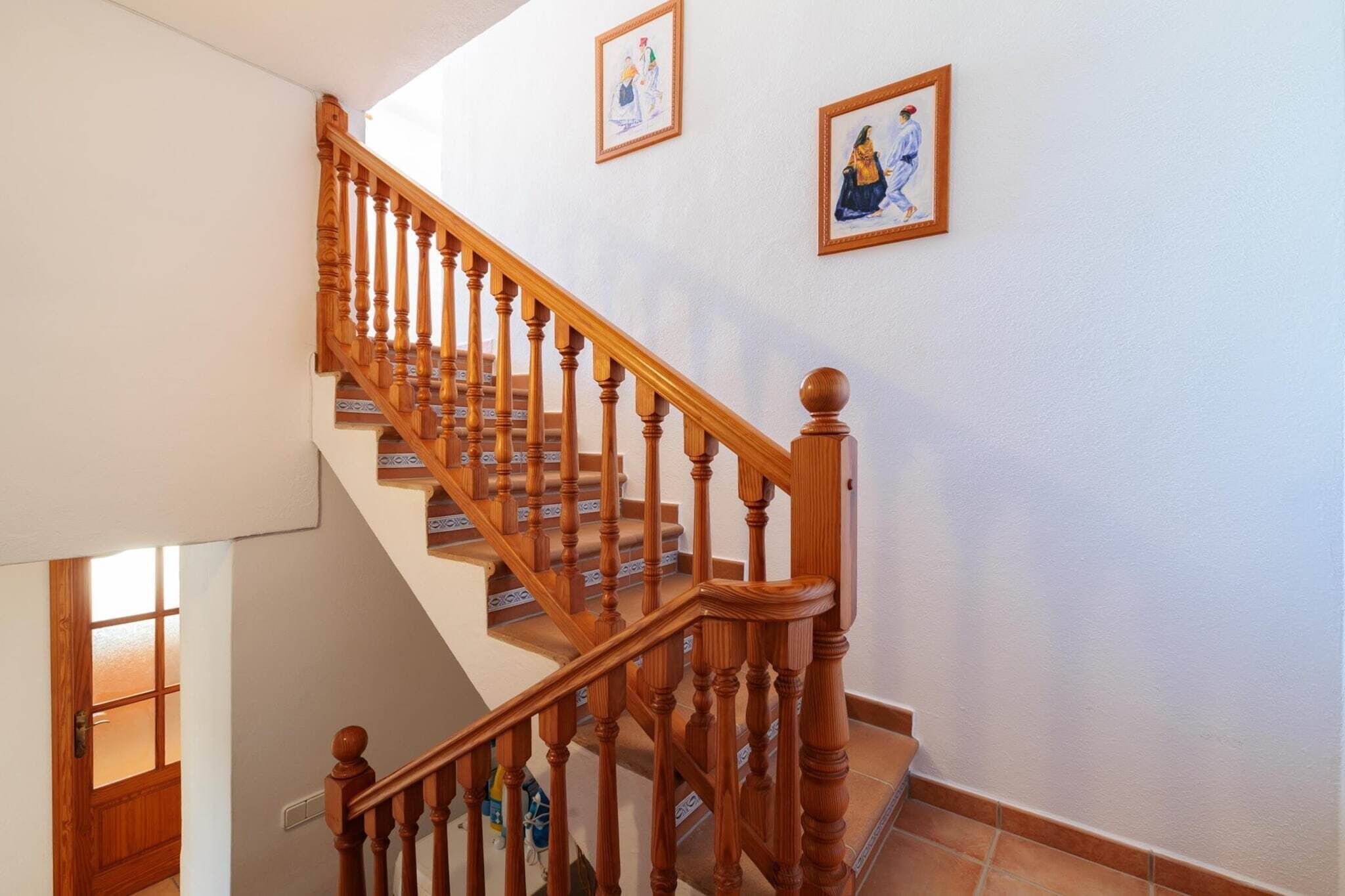 Una scala in legno con corrimano che conduce a un pianerottolo con una porta e una finestra.
