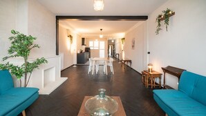 Uma sala de estar moderna com uma mesa de centro de vidro, dois sofás azuis e uma área de jantar ao fundo.