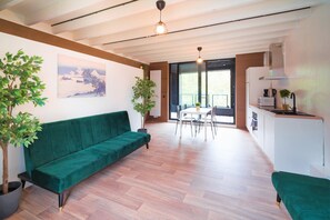 Un espai de vida modern amb un sofà verd, una taula de dinar i una zona de cuina.