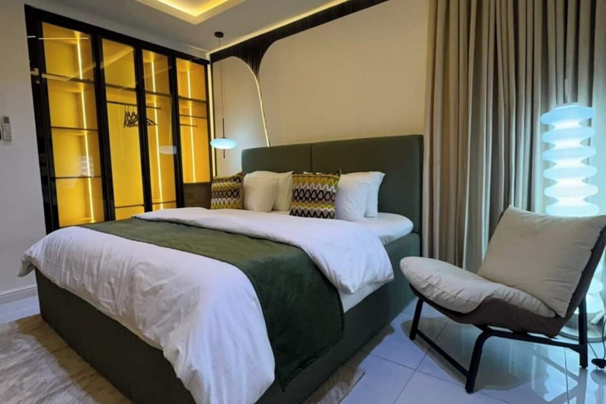 A modern bedroom with a large bed, a chair, and a unique light fixture.