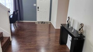 Un pasillo con piso de madera oscura, una puerta blanca y una consola negra decorada con objetos.