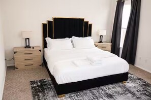 Un lit bien fait, avec du linge de lit blanc, une tête de lit noire et un tapis noir et blanc sur le sol.