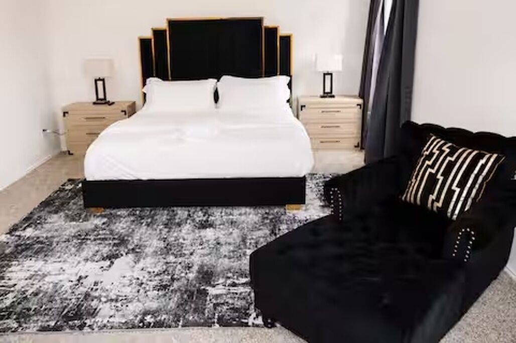 Une chambre à coucher avec un lit, des tables de chevet, un canapé noir et un tapis à motifs.