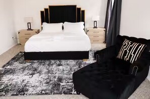 Ein Schlafzimmer mit einem Bett, Nachttischen, einem schwarzen Sofa und einem gemusterten Teppich.