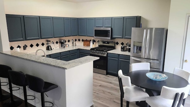 Una cocina moderna con armarios azul oscuro, una isla central con taburetes de bar, una mesa de comedor con sillas y un refrigerador de acero inoxidable.