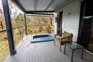 A covered outdoor area with a hot tub, a chair, and a table.