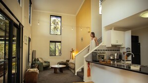 A modern interior with a staircase leading to a kitchen area, a seating area with a coffee table, and a large window providing natural light.