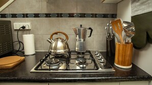 A kitchen with a gas stove, kettle, and various utensils.