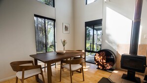 A modern dining area with a wooden table and chairs, a fireplace, and large windows offering a view of the outdoors.